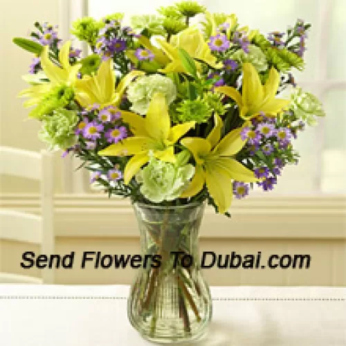 Lys jaunes et autres fleurs assorties disposées magnifiquement dans un vase en verre