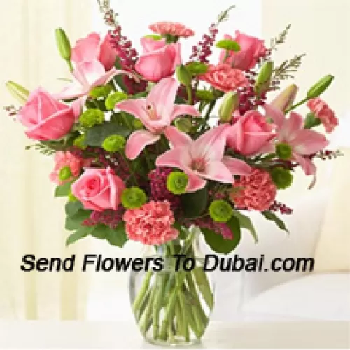 Roses roses, œillets roses et lys roses avec des fougères assorties et des garnitures dans un vase en verre